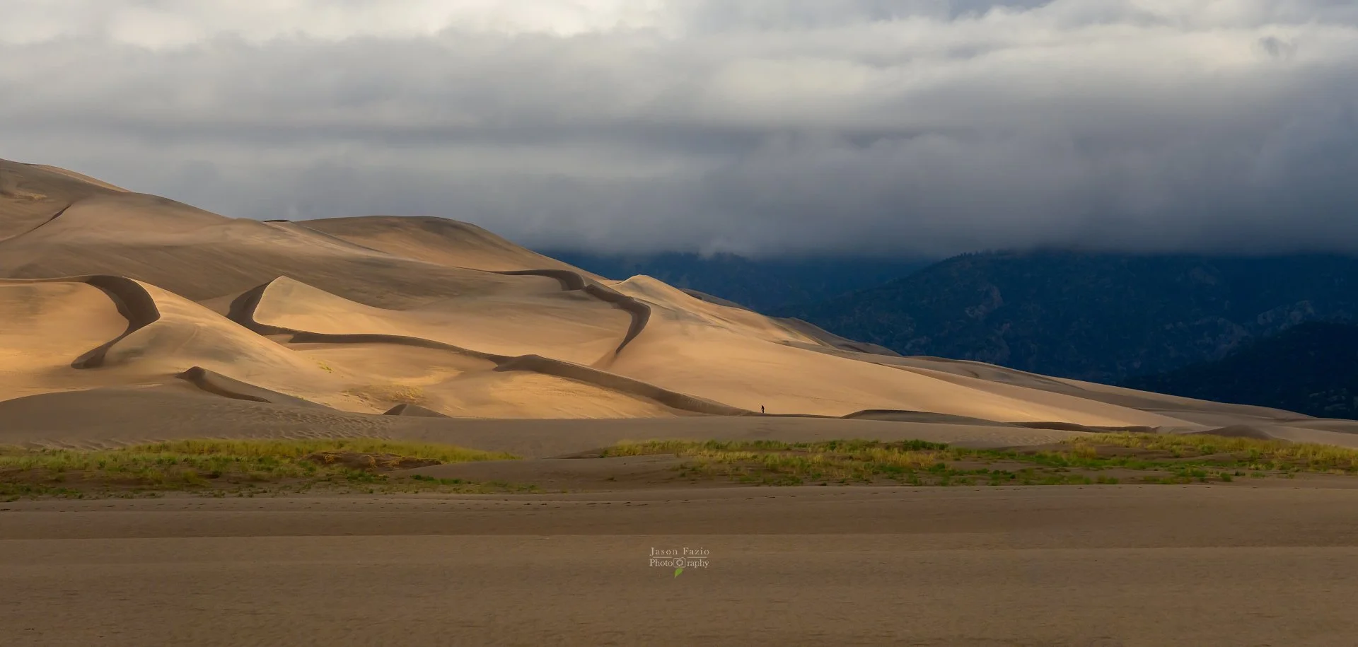Distant sand dunes at the Great Sand Dunes National Park receive side light on a moody Colorado day.