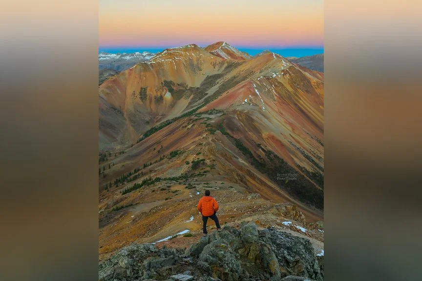 Landscape photographer overlooking the colorful San Juan Mountains at sunrise from Corkscrew Pass near Silverton, Colorado.