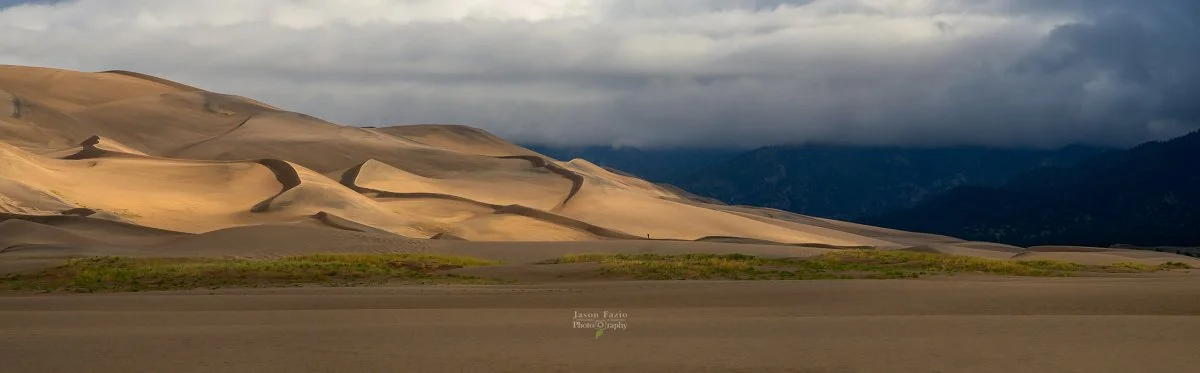 Distant sand dunes at the Great Sand Dunes National Park receive side light on a moody Colorado day.
