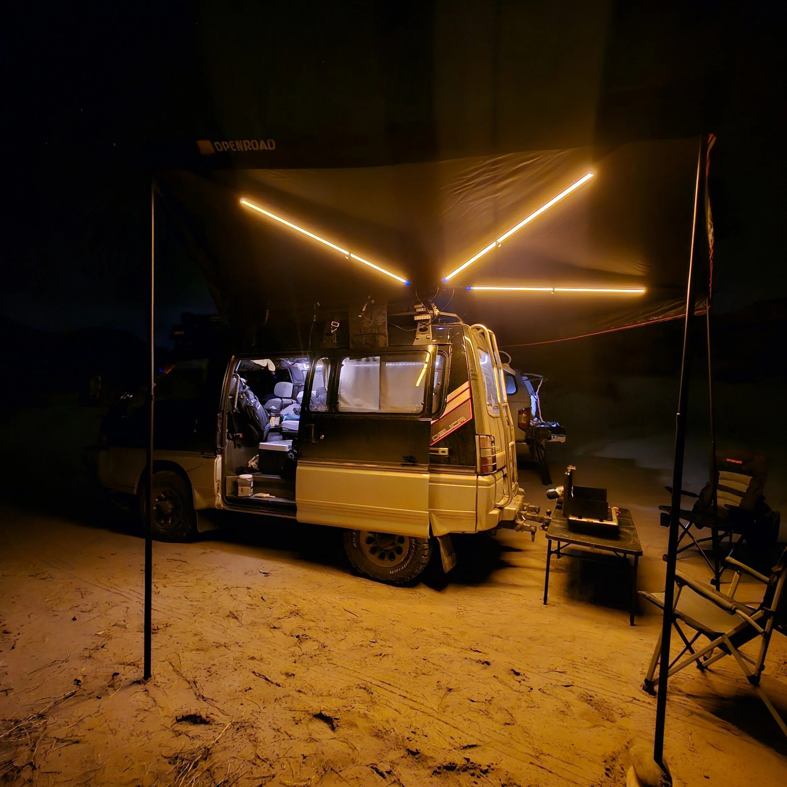 OPENROAD Adventure Series 270-degree awning deployed over a Mitsubishi Delica L300 campsite with integrated LED lights illuminated at night.