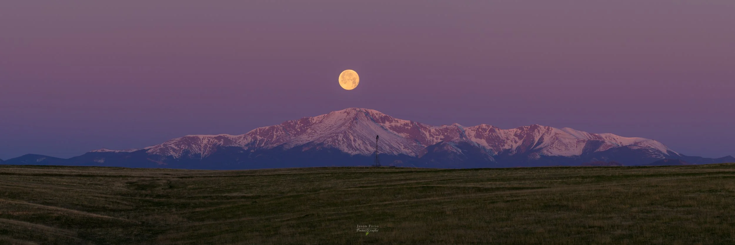 Full moon above snow-covered Pikes Peak during twilight in Colorado.