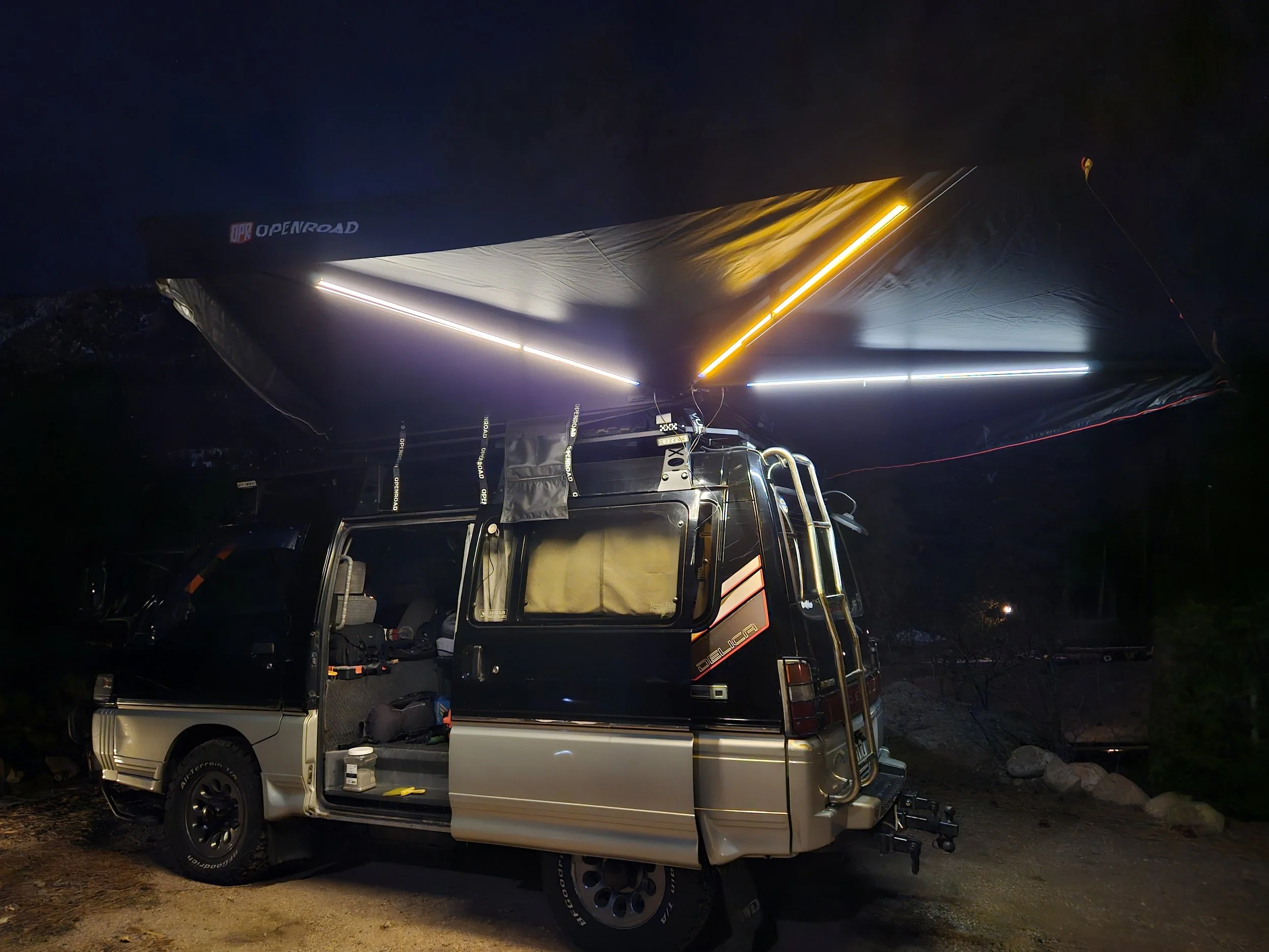 OPENROAD 270-degree Adventure Series awning over a Mitsubishi Delica L300 at night with its warm white, cool white and amber LED lights illuminated.