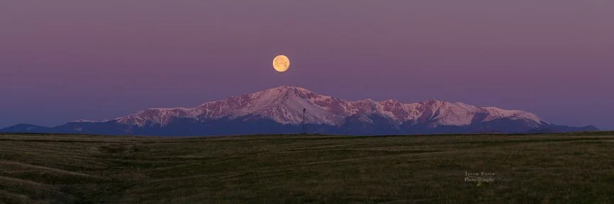 A full moon setting behind Pikes Peak in front of a purple sky just before sunrise