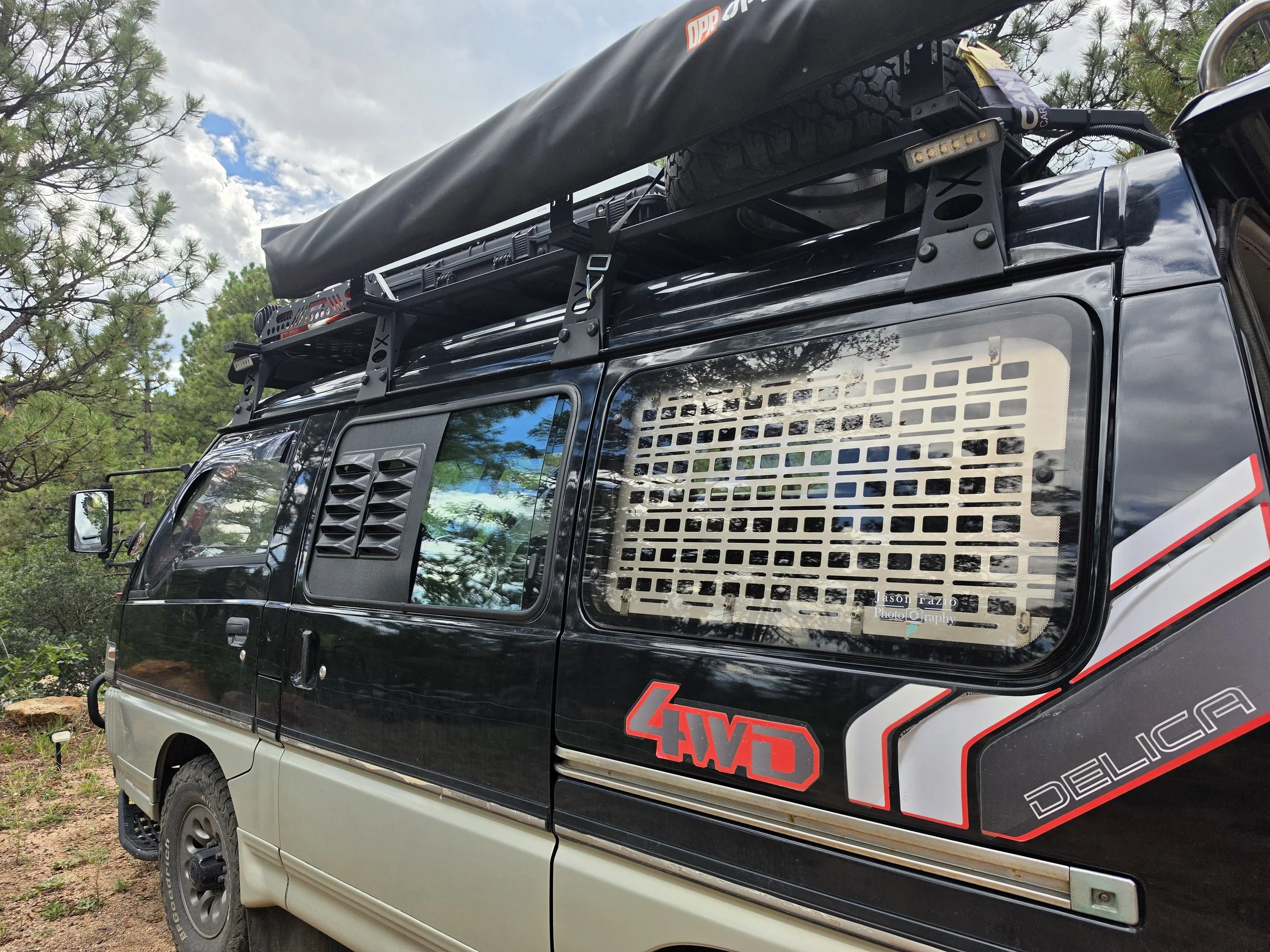 Mitsubishi Delica L300 with screened sliding-window louvers and a MOLLE panel installed in the rear passenger-side window.