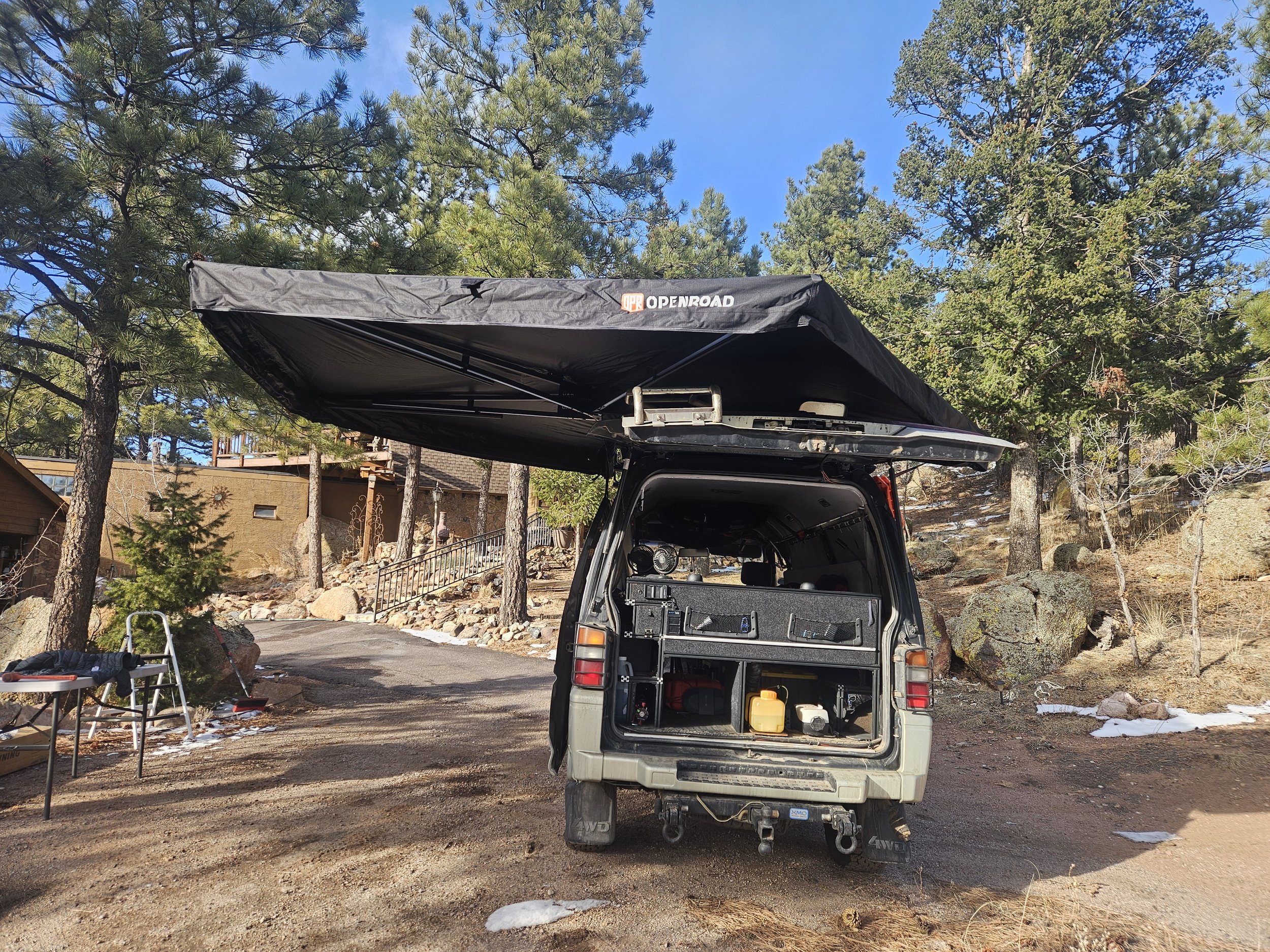 Rear hatch of a Mitsubishi Delica L300 fully open beneath an OPENROAD 270-degree awning mounted higher for additional clearance.