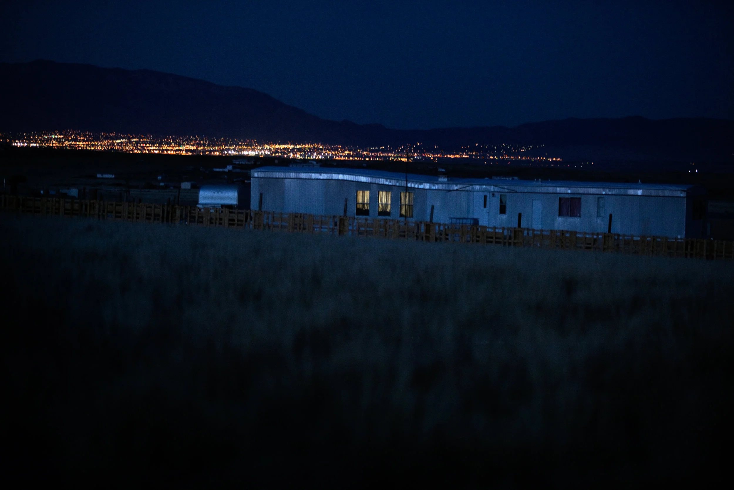 The lights of nearby Albuquerque shine in the distance behind a trailer in Pajarito Mesa, New Mexico on May 24, 2010.