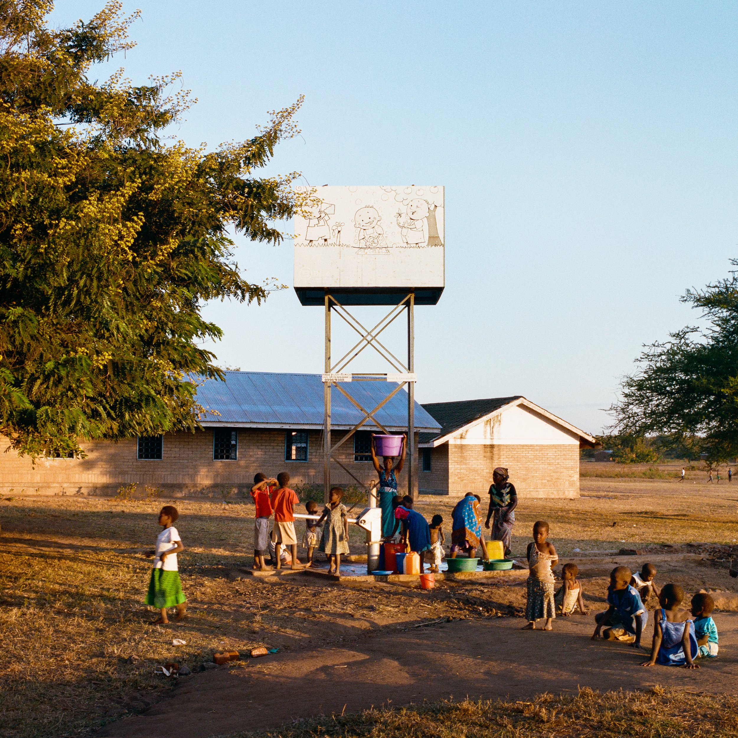  Empty, unused water tower from the site of a broken PlayPump. Thabwa Primary School in Thabwa, Chikhwawa District. Photographed June 9, 2015. The people getting water underneath the tower are using a handpump that does not require use of the tower. 