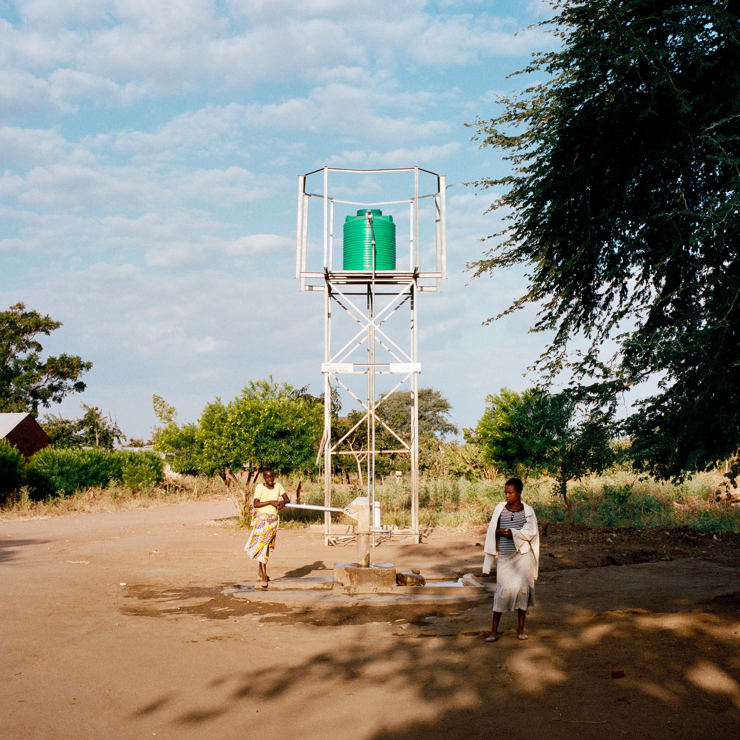  Empty, unused water tower from the site of a broken PlayPump. Nkakawu, Balaka District, Malawi. Photographed June 13, 2015. The people getting water underneath the tower are using a handpump that does not require use of the tower. 