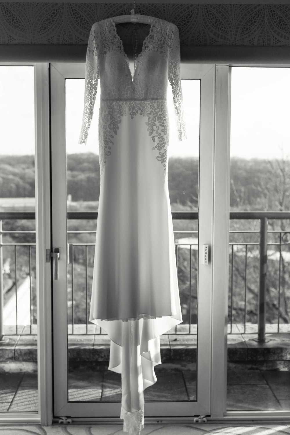 Black and white photograph of brides wedding dress hanging in large window