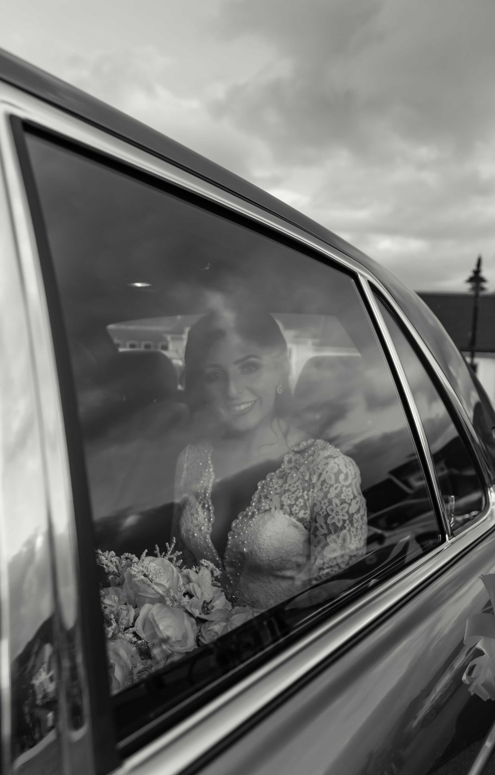 Black and white photograph of brid shot through the window of the wedding car