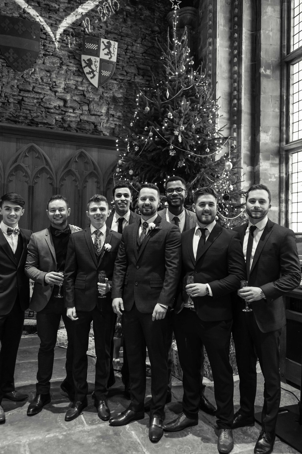 Black and white image of groom with friends next to a large christmas tree at Caerphilly Castle