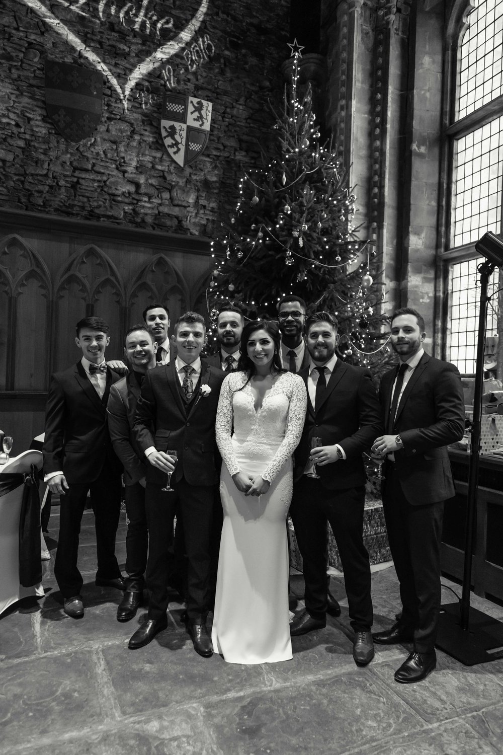 Black and white image of bride groom with friends next to a large christmas tree at Caerphilly Castle