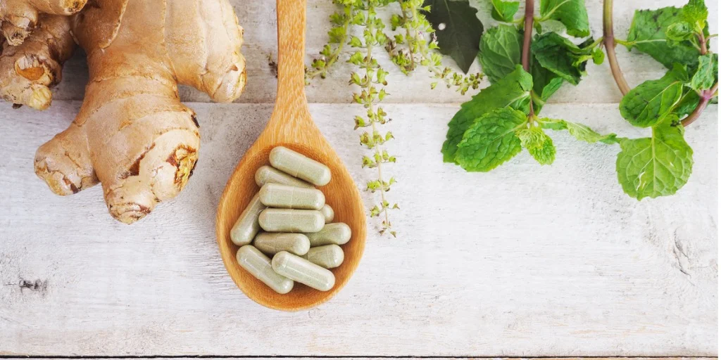 picture of herbal supplement pills on wooden spoon with raw ingredients of ginger root.