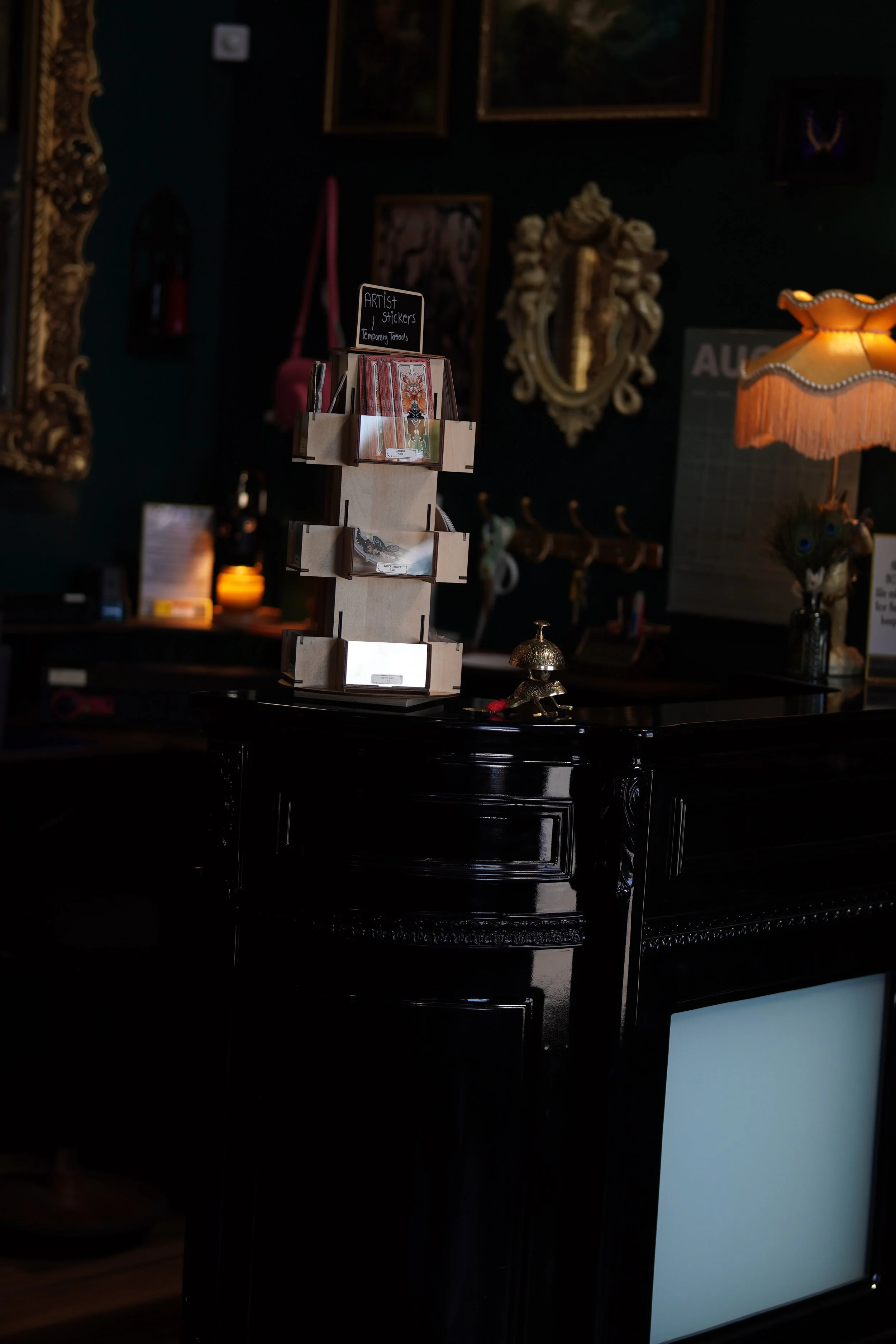 Inside an antique store with ornate mirrors, paintings, and a vintage lamp, featuring a display stand with stickers and art postcards.