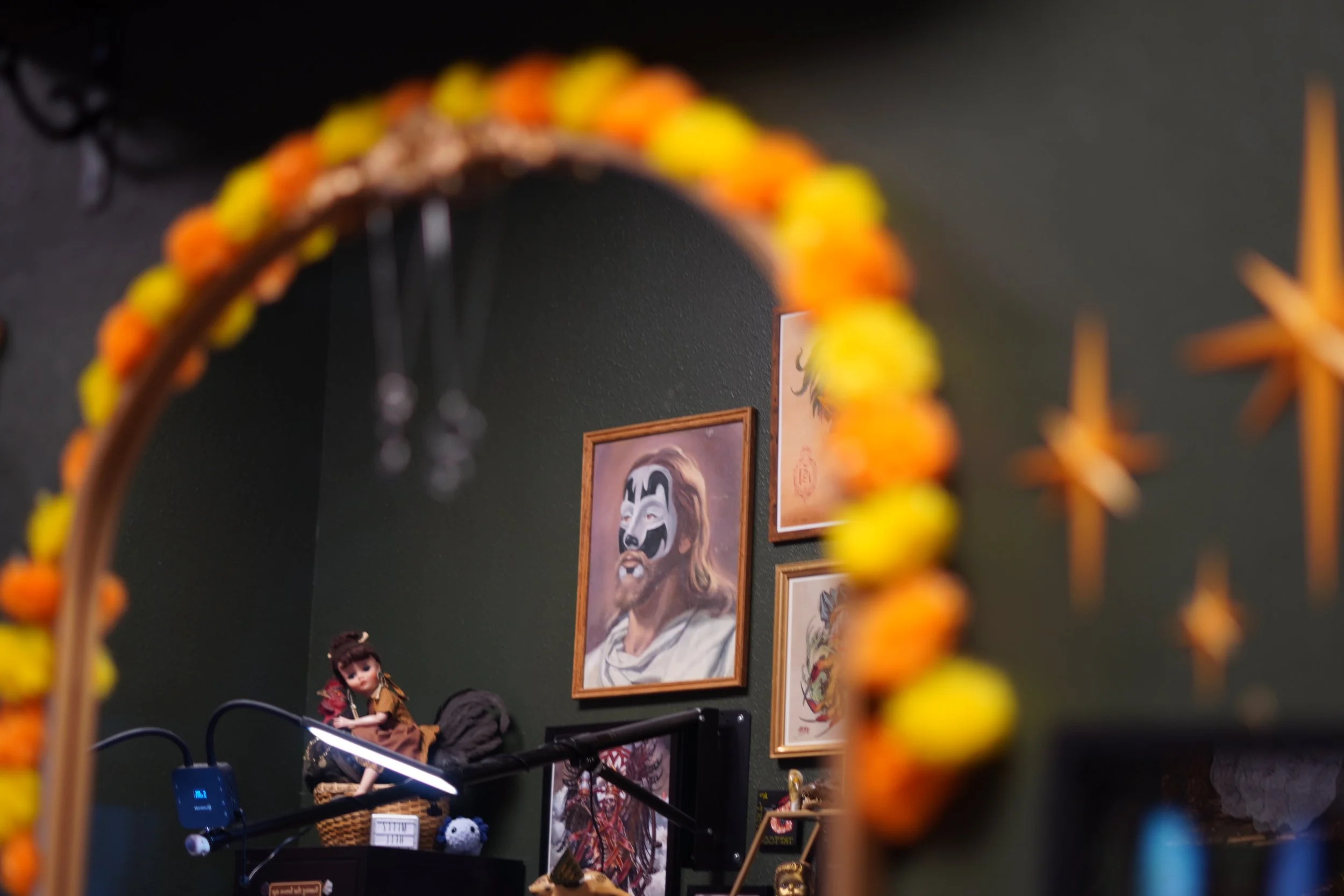 View of a room with framed artwork, plush toys, and dolls on display, partially visible through a decorative frame with yellow and orange beads.