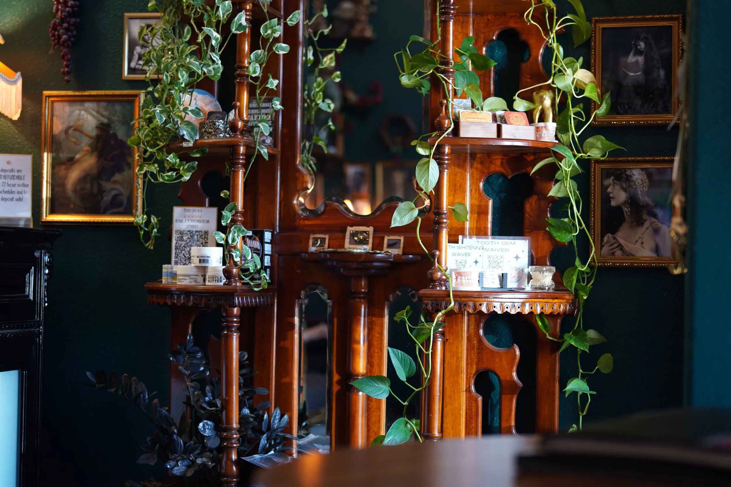 Wooden display shelves with decorative items and green ivy plants, framed historical photographs, and small photos, set against dark green walls.