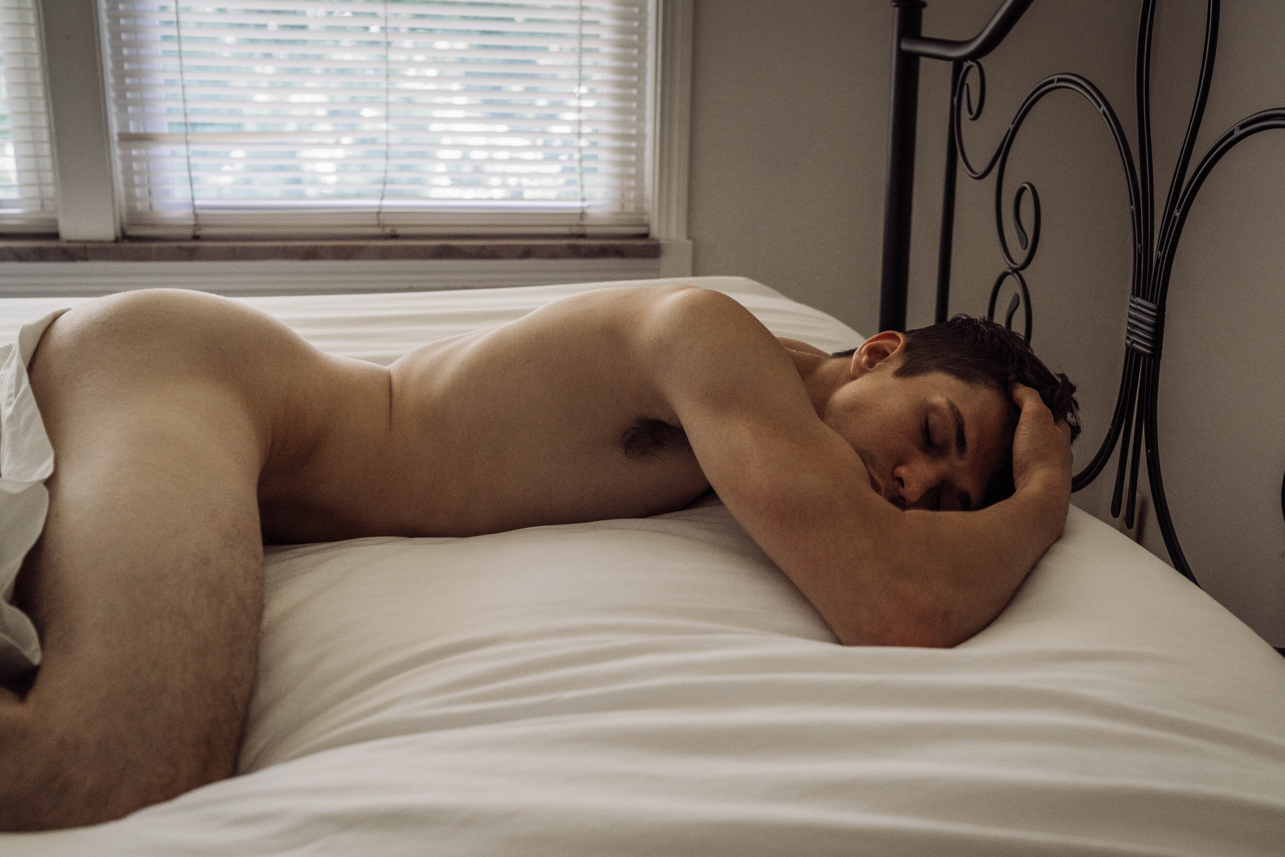 Oklahoma male boudoir photographer white male with brown hair lying in bed nude on stomach with eyes closed