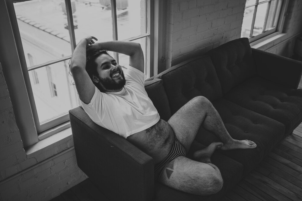 Oklahoma City Male Boudoir Photographer black and white portrait of bearded man in a white shirt sitting on couch laughing