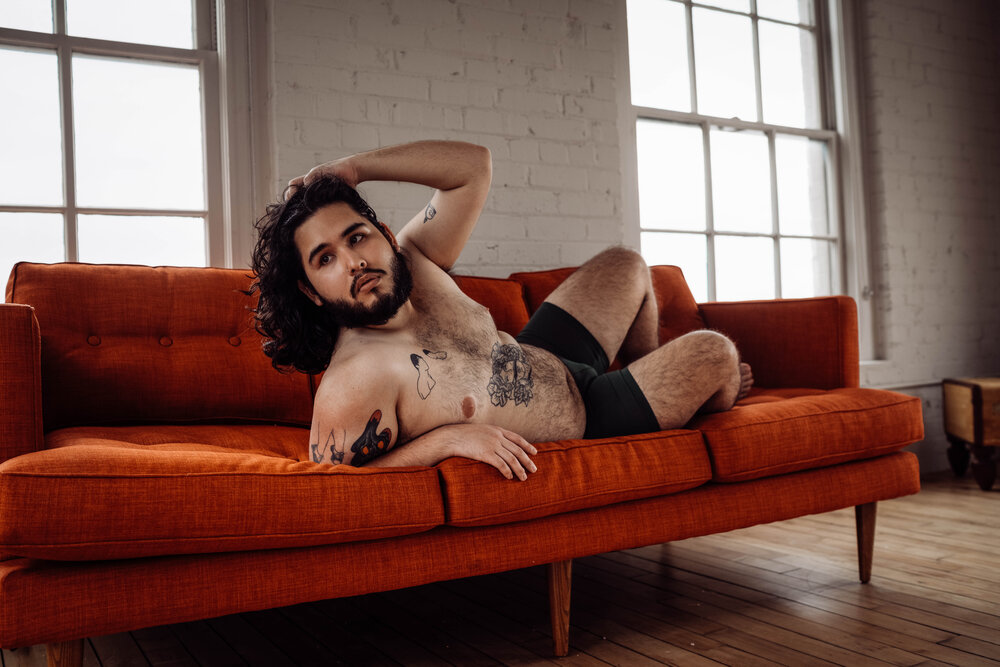 Oklahoma City Male Boudoir bearded shirtless man with tattoos lying on orange couch looking off to the side of camera