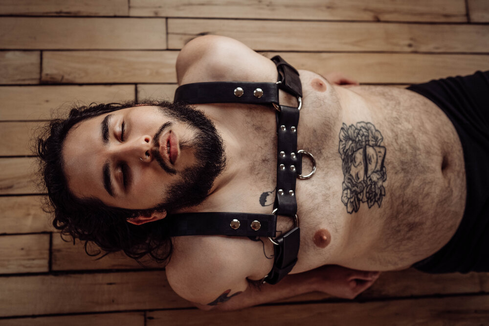 Houston Men's boudoir photographer man lying on ground shirtless wearing a harness with eyes closed