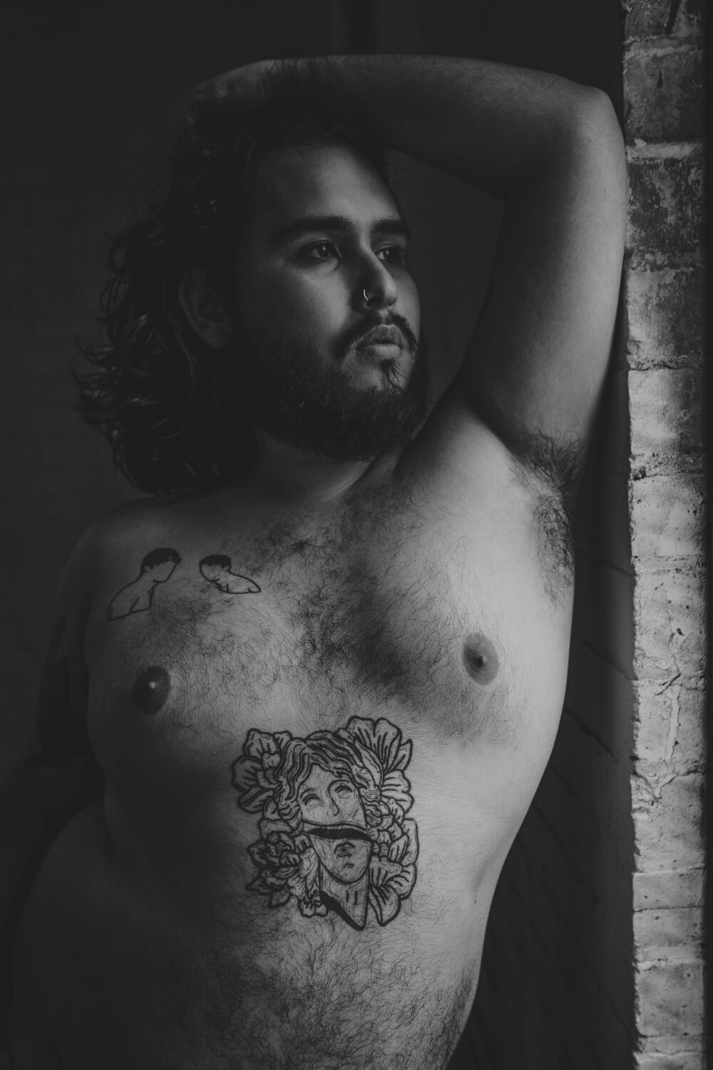 Oklahoma City Male Boudoir black and white portrait of bearded shirtless man with tattoos leaning against brick wall