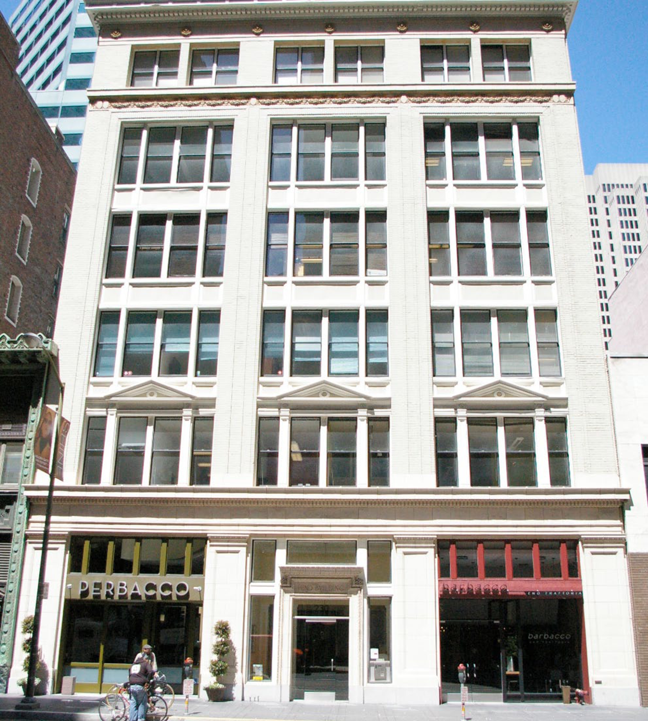 A multi-story commercial building with large windows and decorative architectural elements, housing stores at street level including 'Perbacco'.