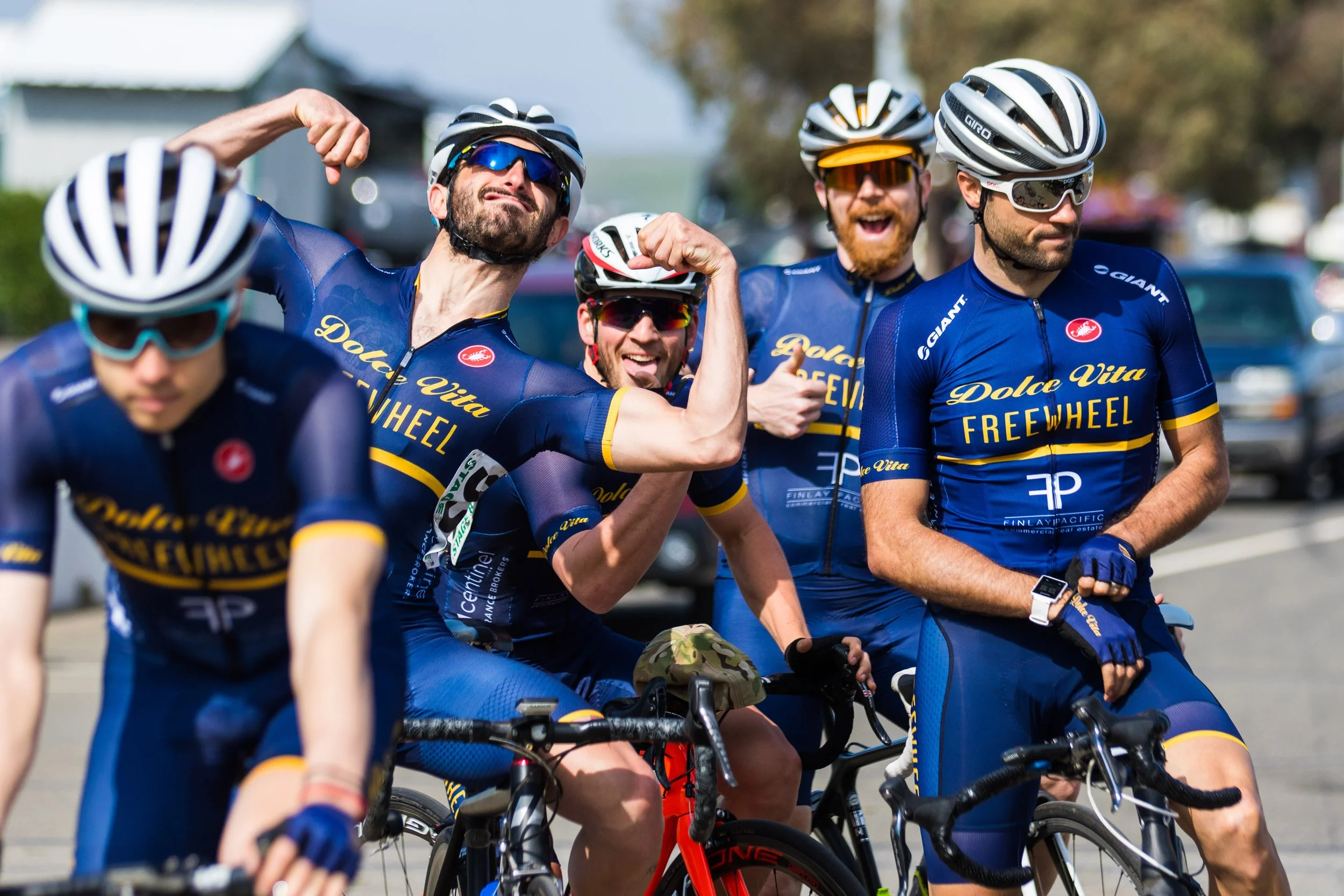 Group of cyclists in blue jerseys with yellow accents, wearing helmets and sunglasses, riding bikes together outdoors during daytime.