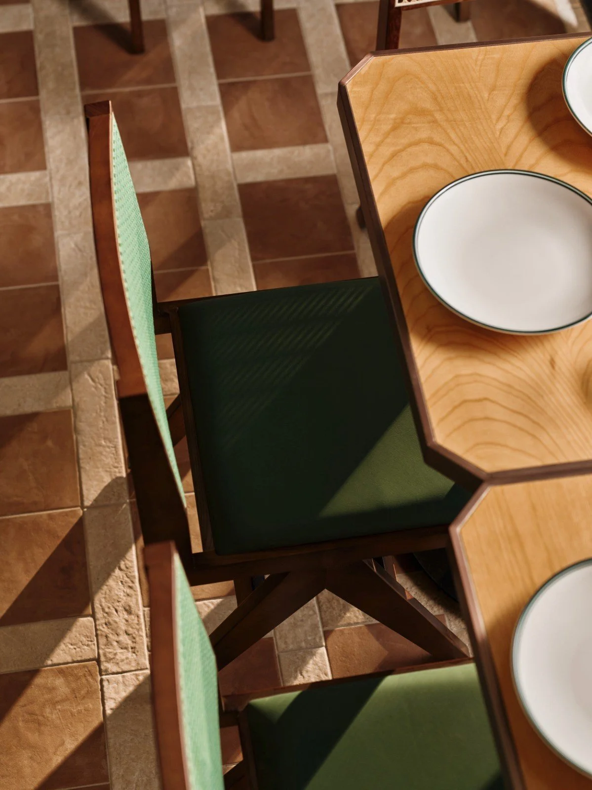 Product of Italy Sydney wooden dining table with green woven chairs and warm tile floor by Al and Co Haus of Design.