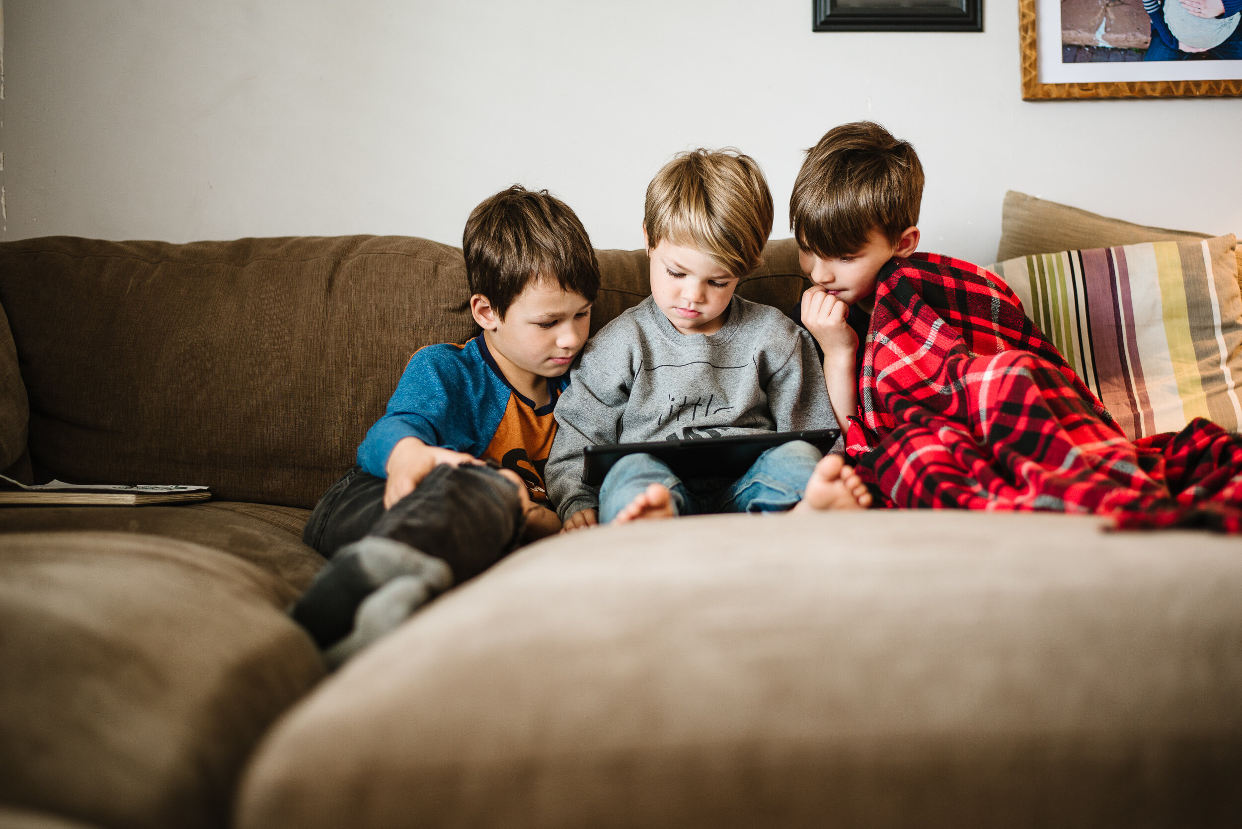 three young brothers huddled together on a brown sectional looking at something on an ipad