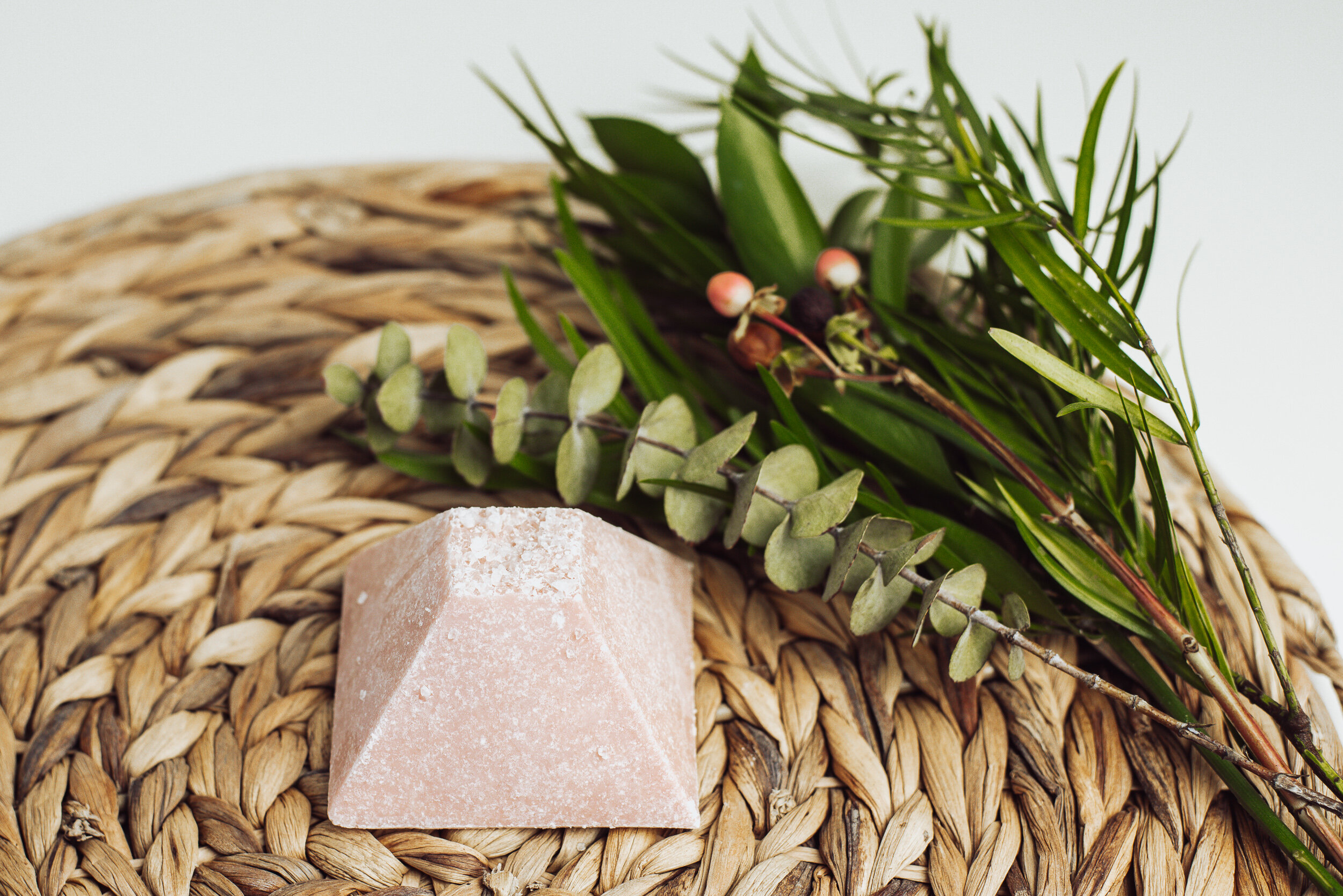 rose pink handmade soap next to a small bouquet of fresh greens on top of a rattan plate placemat