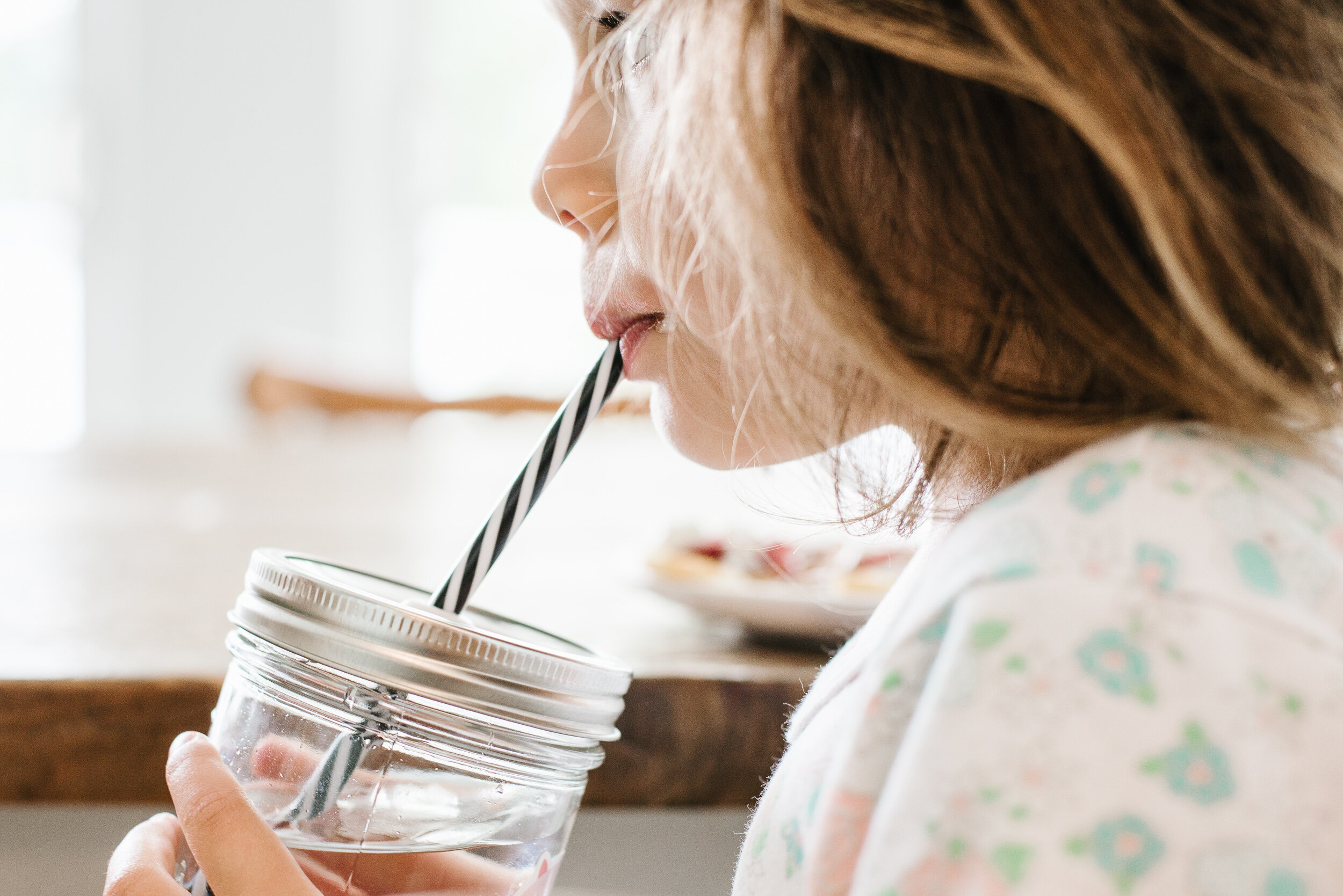 silhouette of a young girl wearing pyjamas and drinking water through a black and white reusable straw