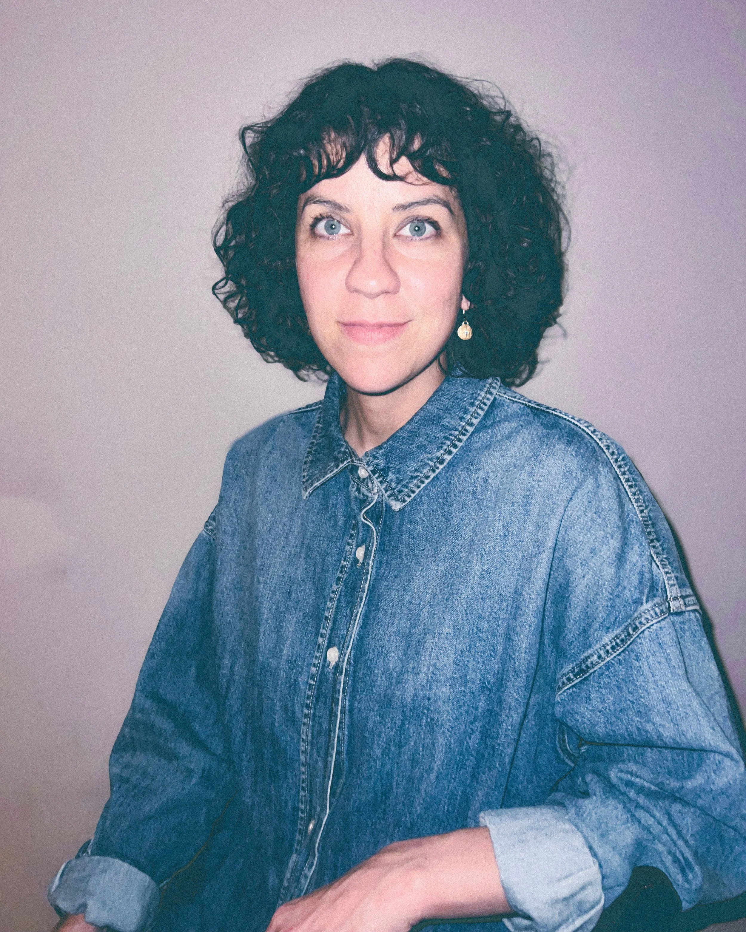 Rachel Witte headshot a white woman with brown hair and blue eyes wears a demon shirt and smiles for the camera