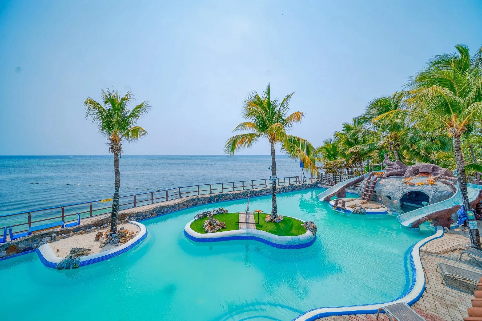 Resort pool area with a lazy river, water slide, palm trees, and ocean in the background.