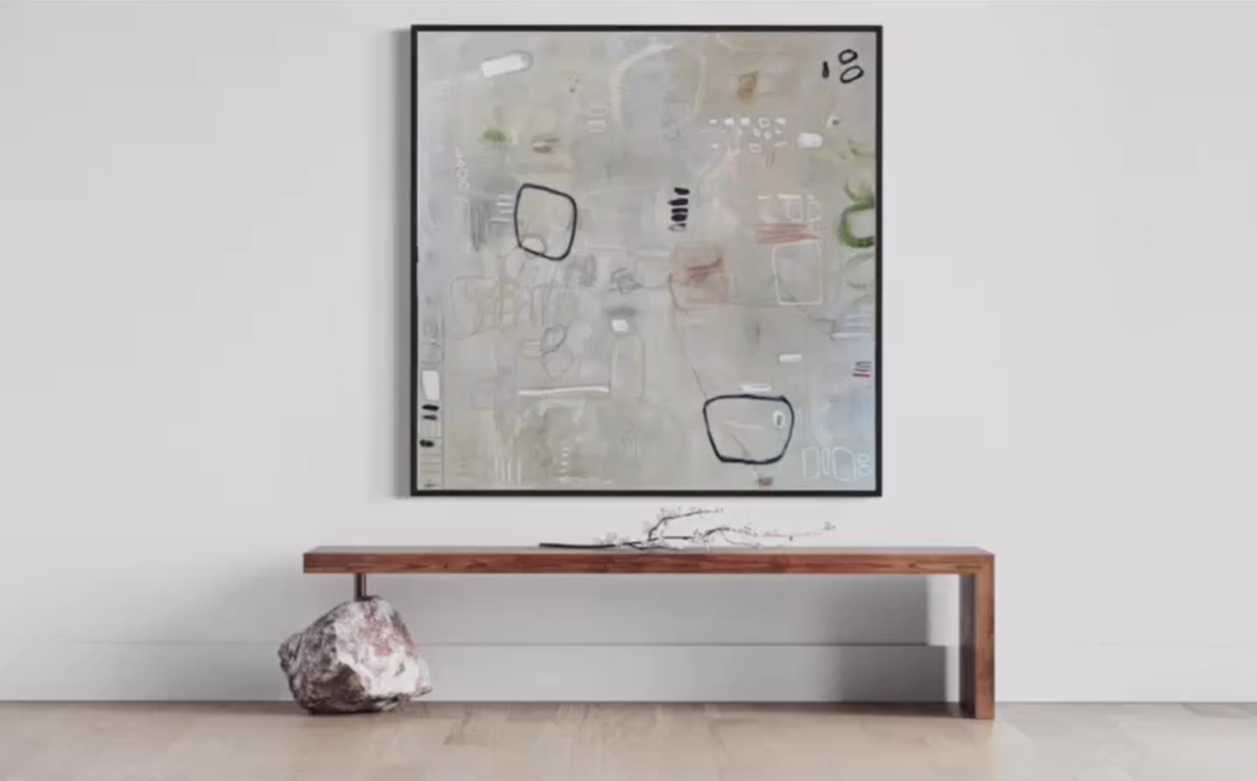 A large abstract wall art piece on a white wall, with a wooden bench below it. The art features various shapes and lines in muted colors with some black accents.