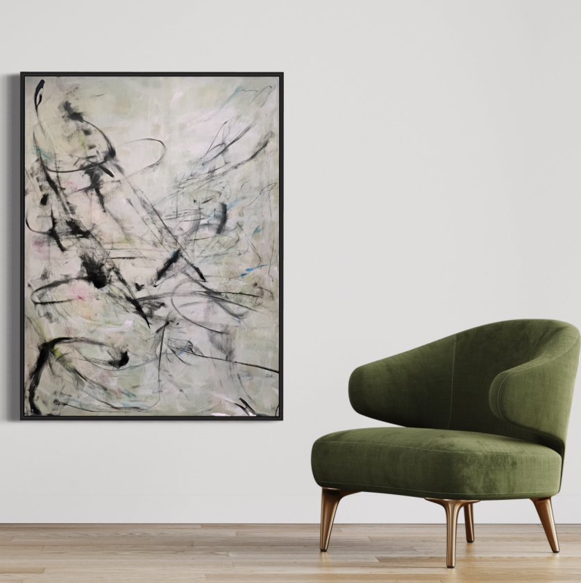 Abstract painting with black, pink, and blue strokes hanging on a white wall, next to a green upholstered armchair on a light wood floor.