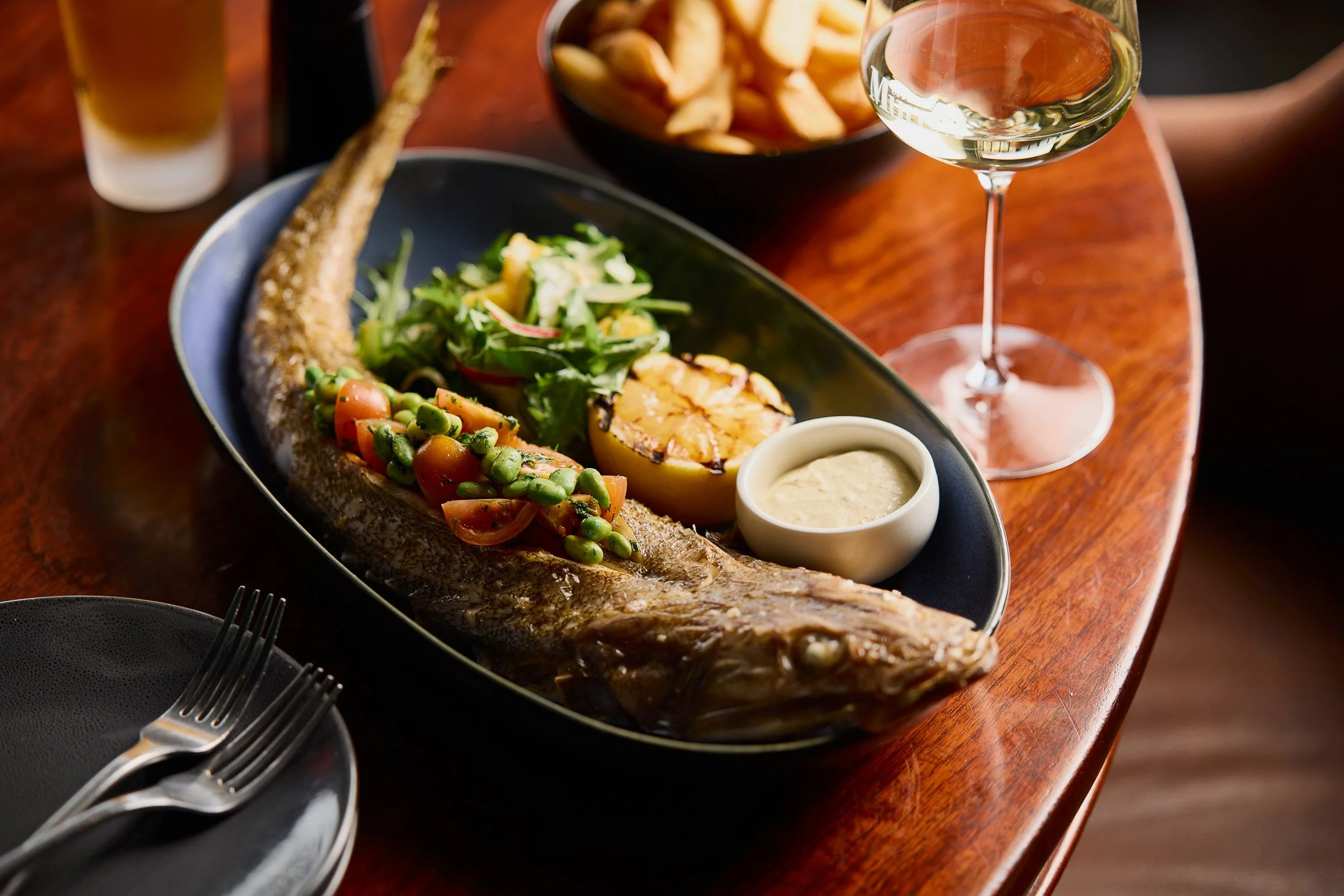 A whole flathead fish on a plate, with a bean salsa served along it's back, accompanied by salad, tartare sauce and a half grilled lemon.