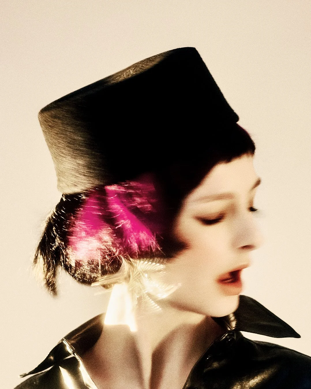 Intimate close-up portrait from an exclusive PAP Magazine editorial, showcasing a model with bold pink feathers and sleek black hat against dramatic lighting. Shot by a celebrated London fashion photographer, this worldwide-renowned commercial and ed