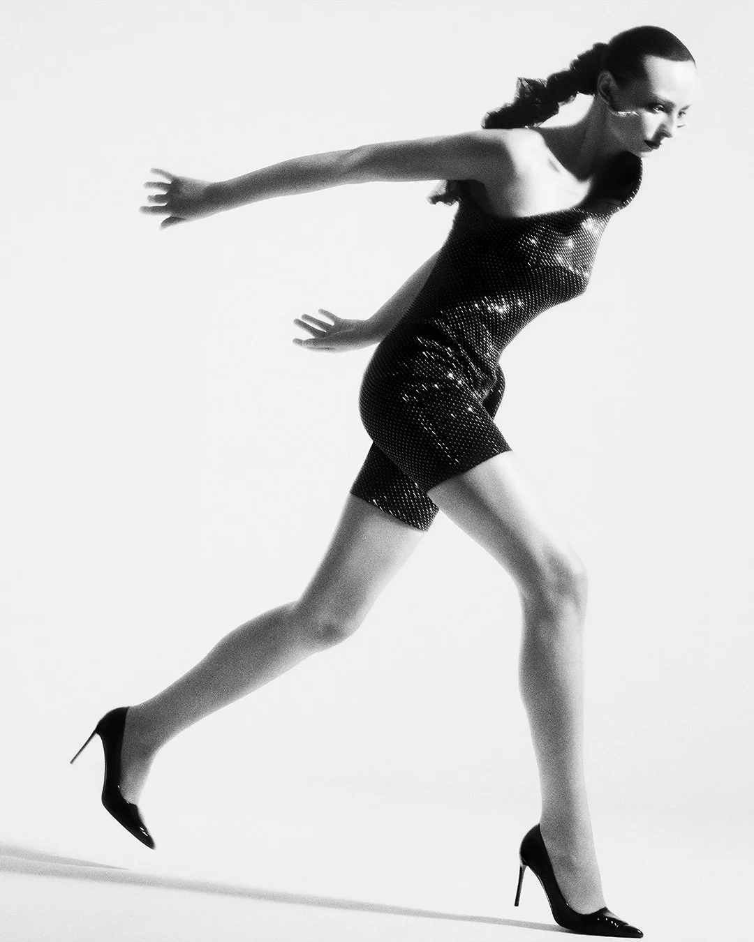 High-energy black-and-white editorial of a model with braided ponytail swinging a large sequined accessory, captured in full motion by a celebrated London fashion photographer. This worldwide-renowned commercial and editorial photographer excels at c