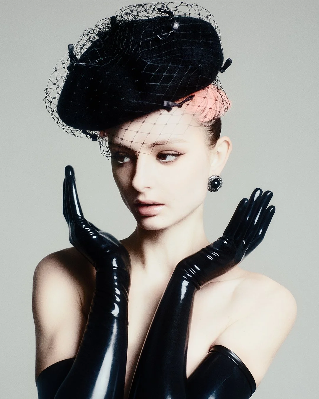 Elegant black-and-white studio portrait of a model wearing a dramatic black veil hat and long glossy latex gloves, captured in profile for an exclusive editorial published in PAP Magazine. Shot by a renowned London fashion photographer, this internat