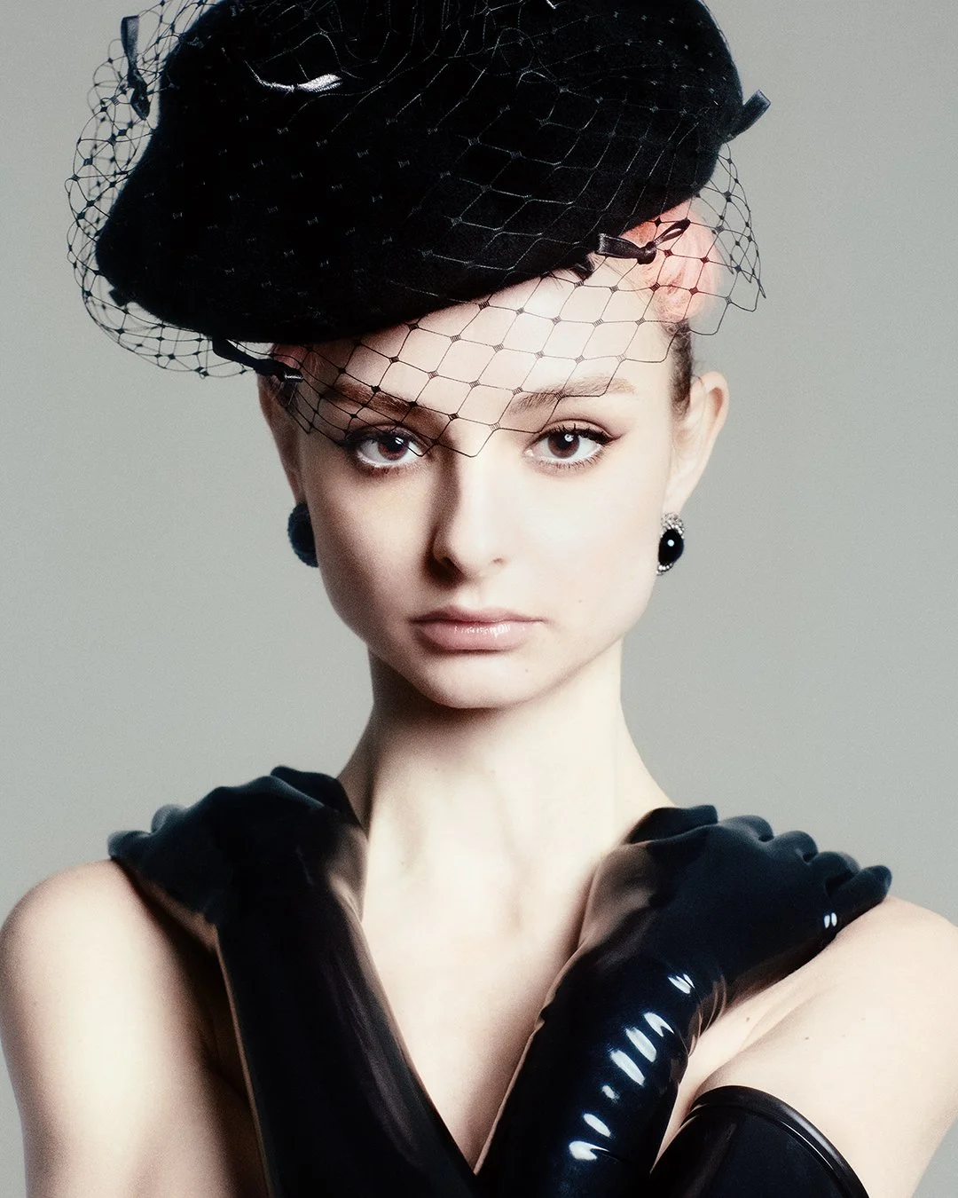 Striking close-up from an exclusive PAP Magazine editorial featuring a model in a black mesh veil hat and shiny long gloves, gazing directly at the camera. Photographed by a leading London-based fashion photography specialist, this global visionary d