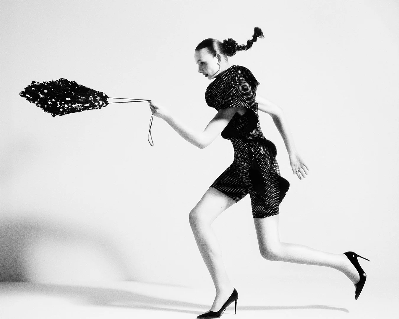 Bold black-and-white fashion portrait of a model in a sequined mini dress running with a large sparkling accessory in hand, shot by a renowned London-based editorial photographer. This global commercial photography specialist is known for dynamic, ci