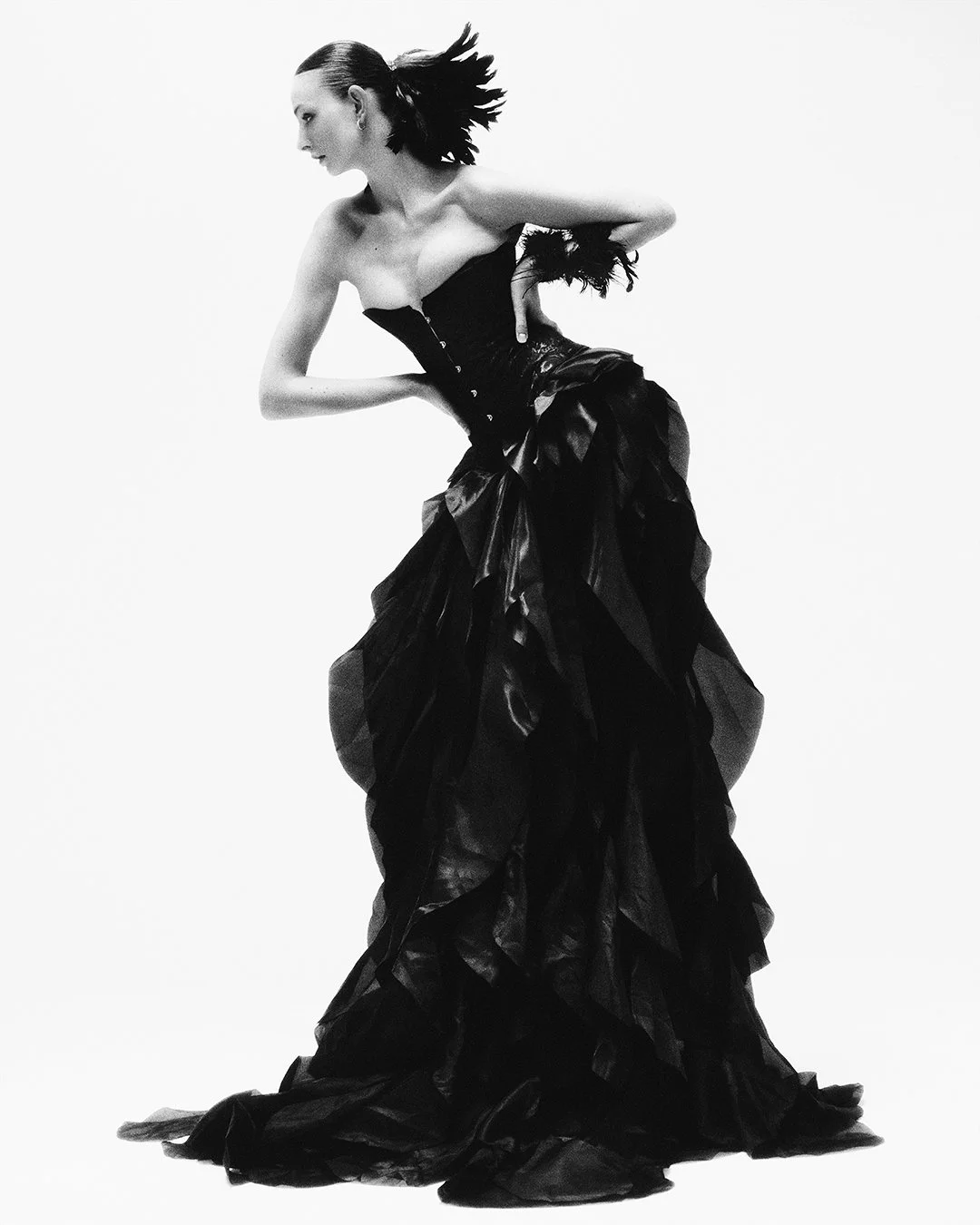 Powerful black-and-white fashion portrait of a model in a dramatic strapless corset gown with cascading ruffles and feather details, captured by a renowned London fashion photographer. This international editorial and commercial photographer delivers