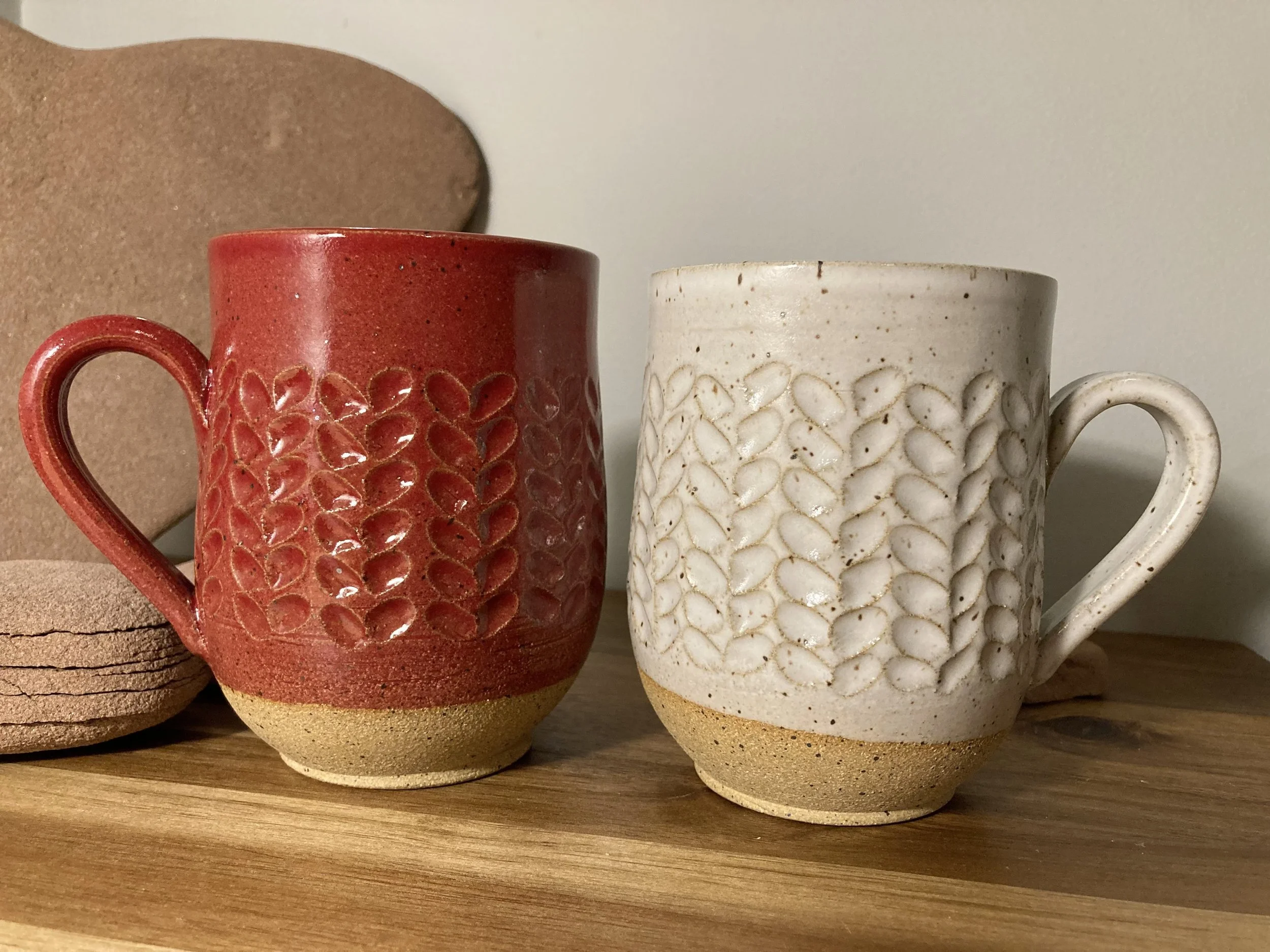  A red and a white pottery mug on a wooden surface 