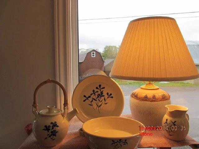  Bowls and tea kettle on a table in front of a wall &amp; window, with a lit up lamp on the right of the table 