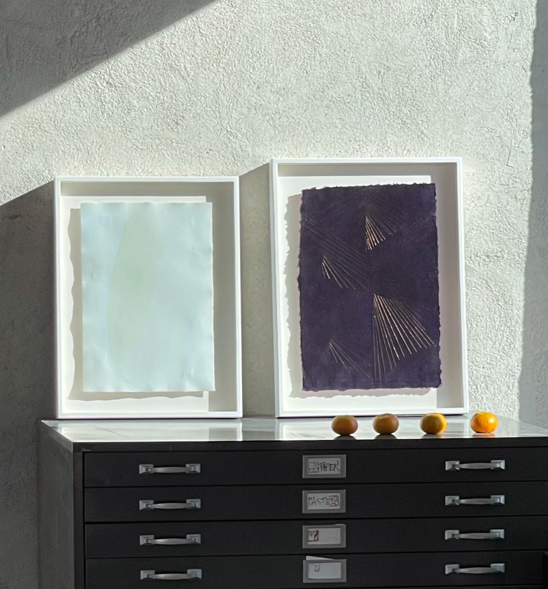 Framed pastel artworks leaning on a flatfile.