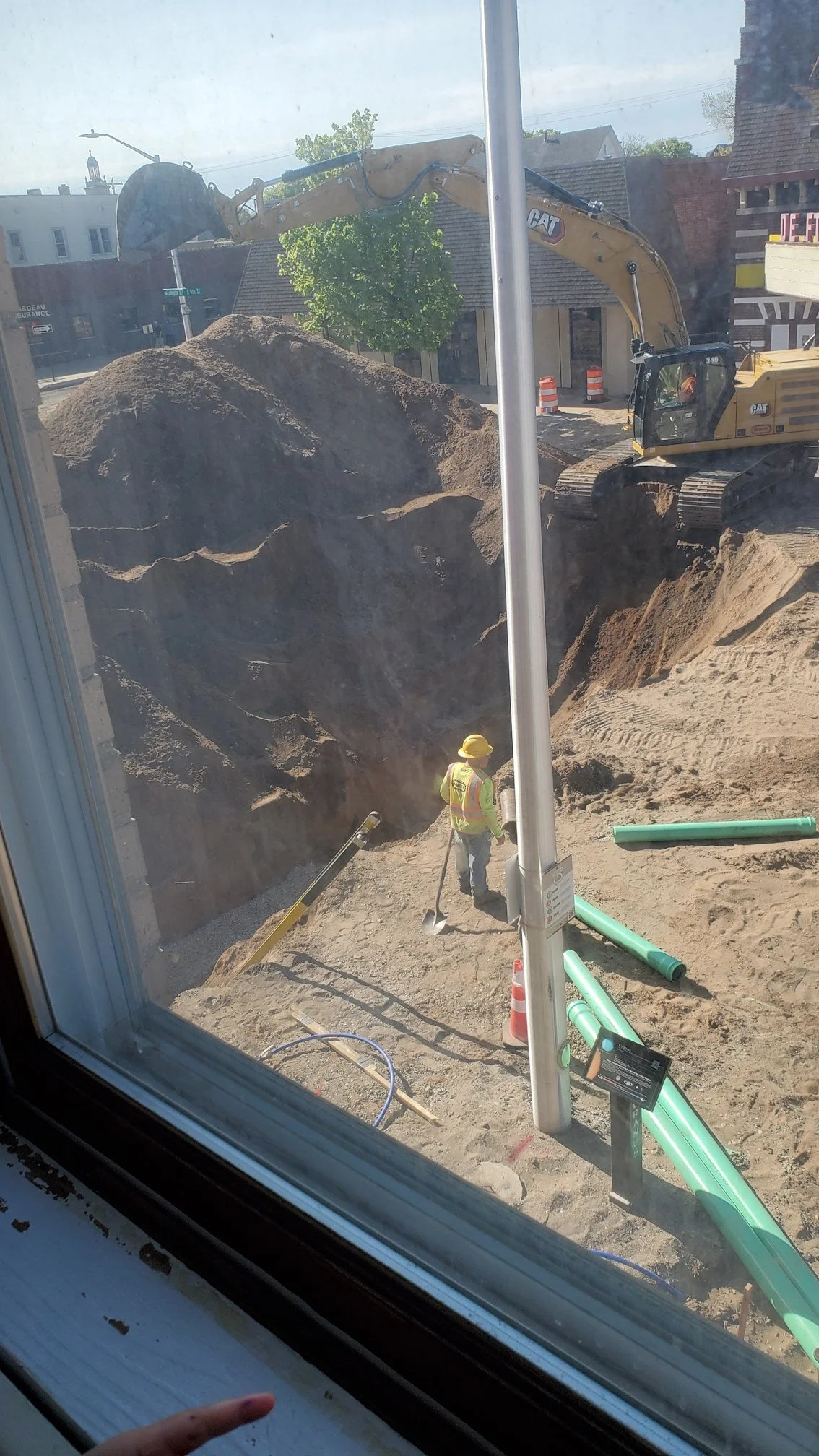 A large whole in the sandy soil where Ludington street used to be, with an excavator next to it actively digging it out