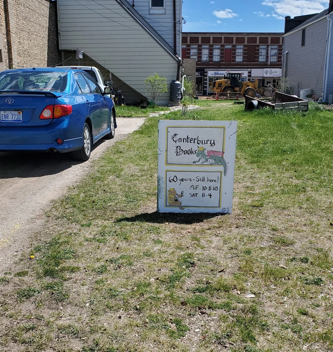 A small, hand-painted sign stuck in the ground behind the Canterbury Book Store that reads "Canterbury Books"