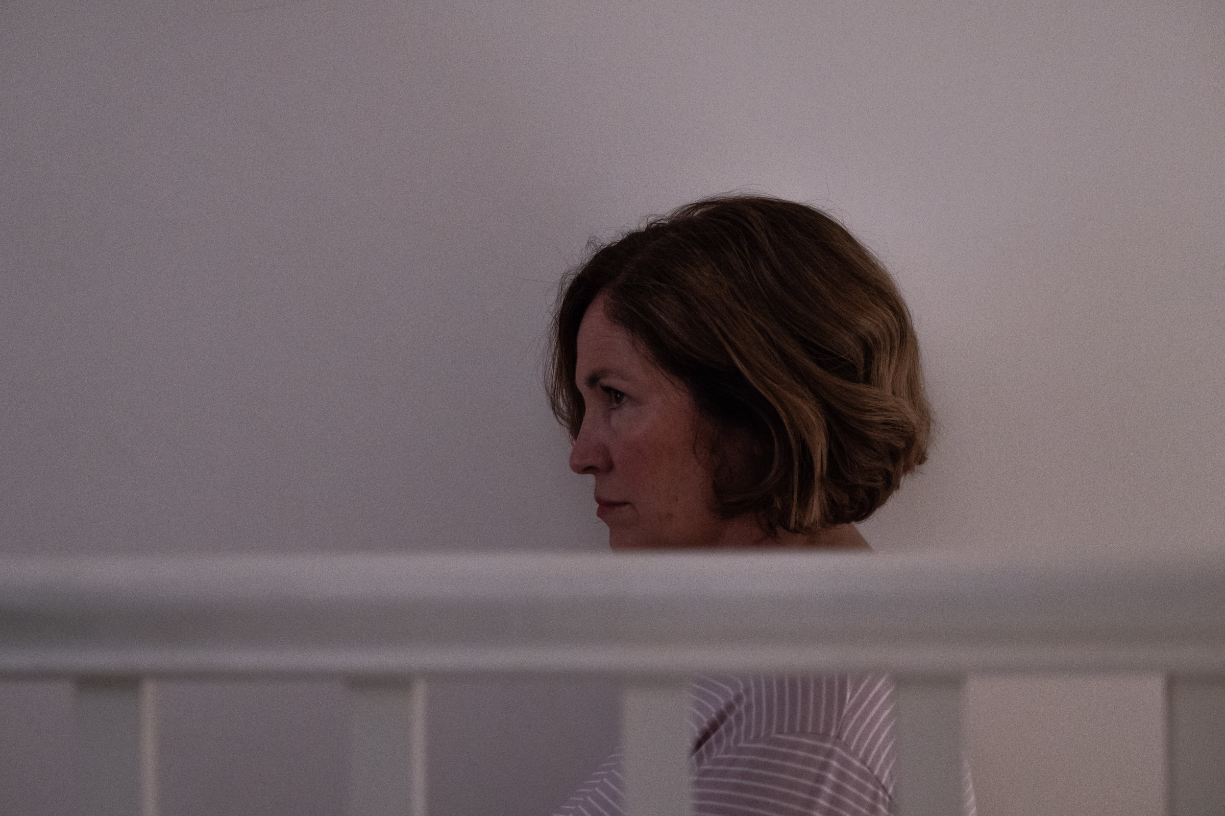 Andrea Irvine stands behind a bannister on the top of the stairs.   Still from Pills. 