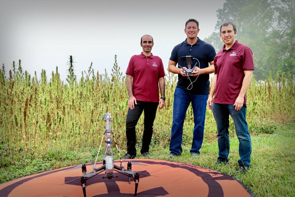 Virginia Tech researchers Hosein Foroutan (left), David Schmale (middle), and Shane Ross (right) standing behind their drone, which is mounted with a 3D-printed sampling device to collect and analyze hemp pollen. (Photo credit: Alex Crookshanks)