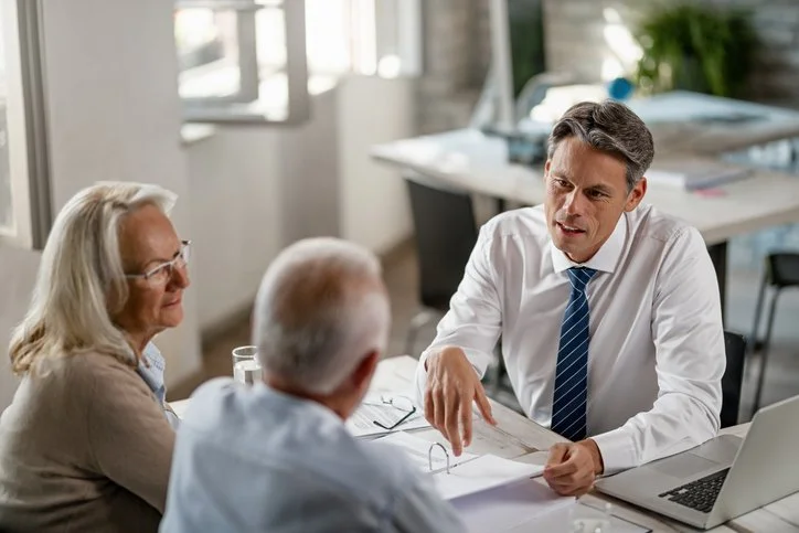 Older professional man in meeting with senior couple, sitting at desk, looking over paperwork